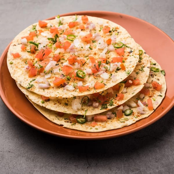 Three stacked papadums topped with diced tomatoes, onions, green chilies, and herbs on a brown plate.