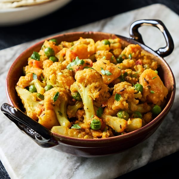 A close-up of a bowl of Indian aloo gobi, a curry with cauliflower, potatoes, and peas.