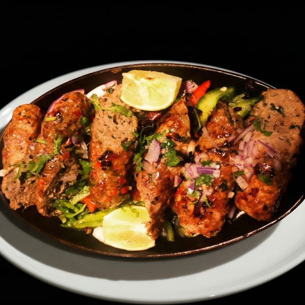 Dhabewala Indian Shack's seekh kebabs, garnished with lime, cilantro, and red onions, served on a dark platter.