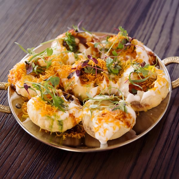 A golden tray of Indian Dahi Puri, topped with yogurt, chutneys, sev, and microgreens.