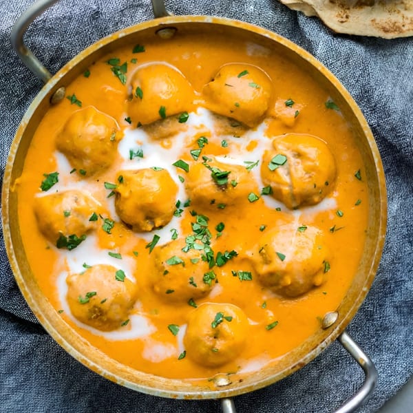 Malai Kofta, Indian cheese and vegetable dumplings in a rich, creamy orange sauce, garnished with cilantro.
