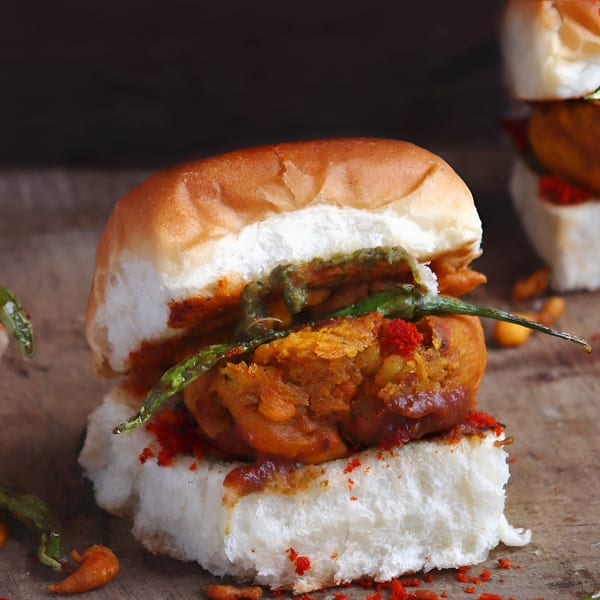 Close-up of a vada pav, an Indian potato fritter in a bun, with green chili and red spice.