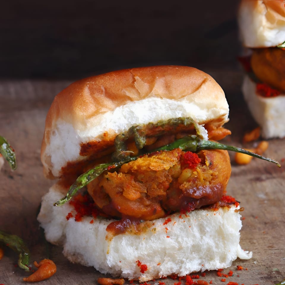 Close-up of a vada pav, an Indian potato fritter in a bun, with green chili and red spice.