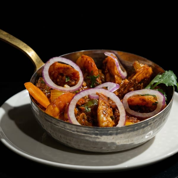 Indian shrimp curry with red onions and cilantro in a hammered metal bowl with a brass handle.